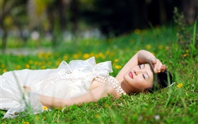 Vestido blanco Asia niña acostada de hierba