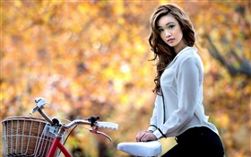 La muchacha asiática y en bicicleta en otoño