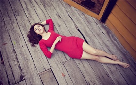 Muchacha asiática que miente en suelo de madera, vestido rojo