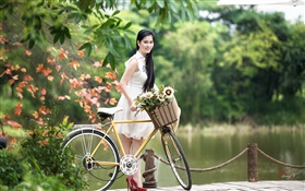 Muchacha de la sonrisa asiática, vestido de blanco, bicicleta, parque